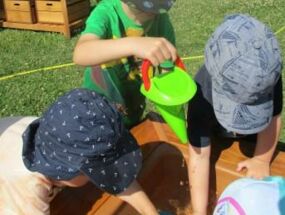 Kinder spielen mit Trichtern und Schüsseln am Wasserbecken