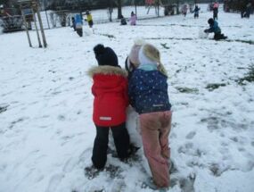 Kinder spielen im Schnee, drei Kinder bauen Schneemann