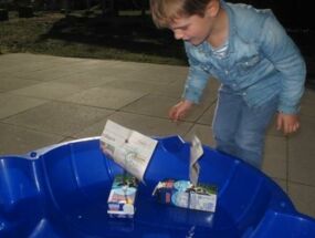 Ein Junge lässt ein Boot aus Zeitung und einer Milchtüte fahren