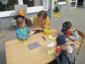 Kinder und Erzieherin sitzen am Tisch und basteln