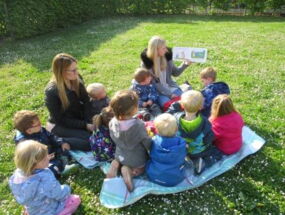 Kindergruppe sitzt auf Wiese und schaut Hühnerbuch